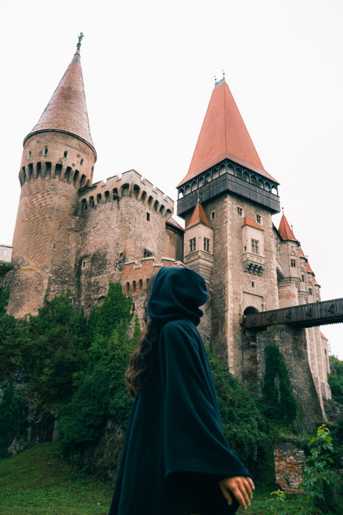 Ragazza con mantella da strega davanti a uno dei castelli più belli della Transilvania